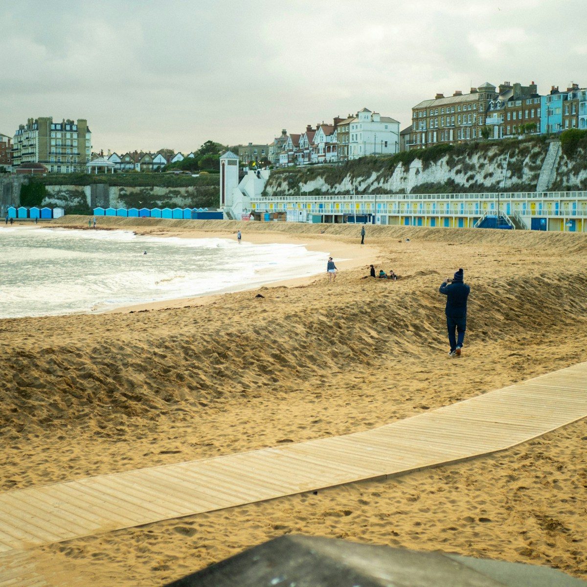 A lone figure walks on a sandy beach path.